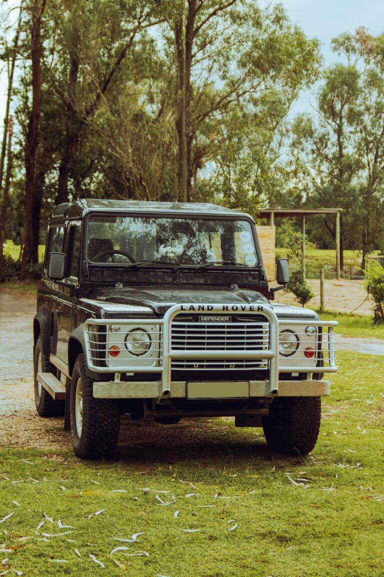 A rugged Land Rover Defender parked amid lush greenery on a sunny day.