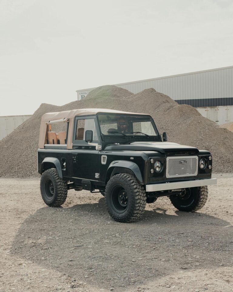 Classic Land Rover Defender parked in an industrial area with gravel mounds.