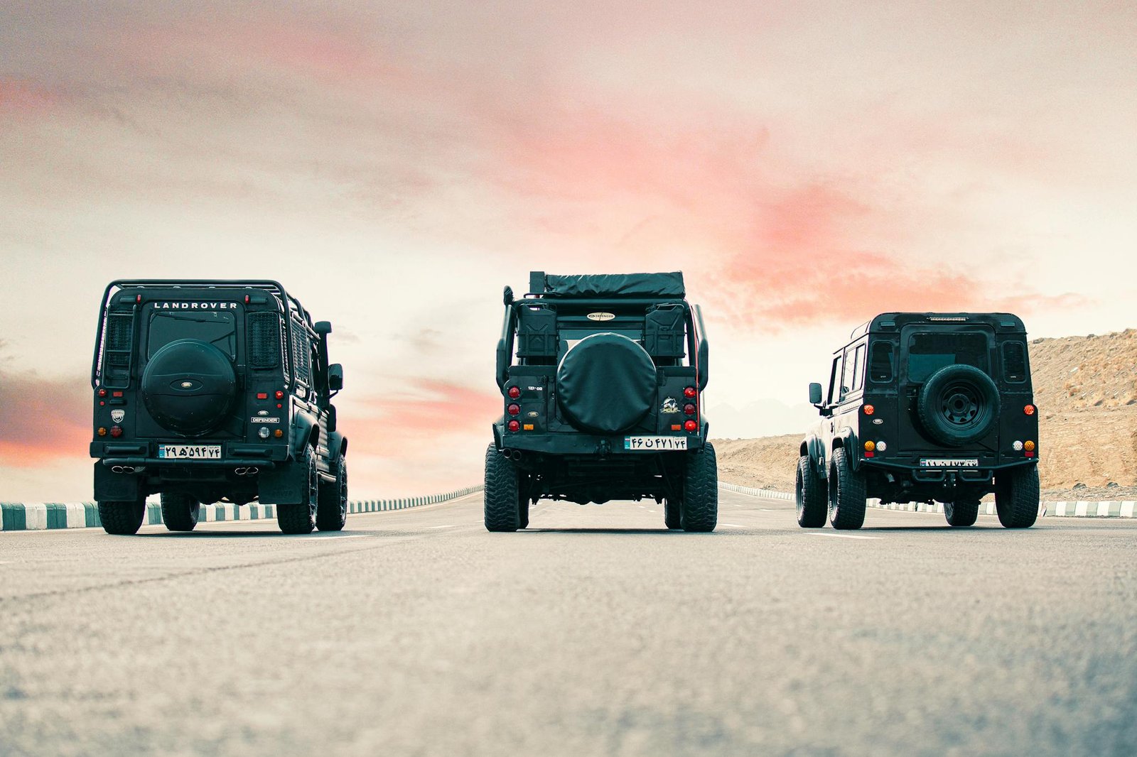 Three Land Rover vehicles parked on an open road with a beautiful sunset sky in Mashhad, Iran.